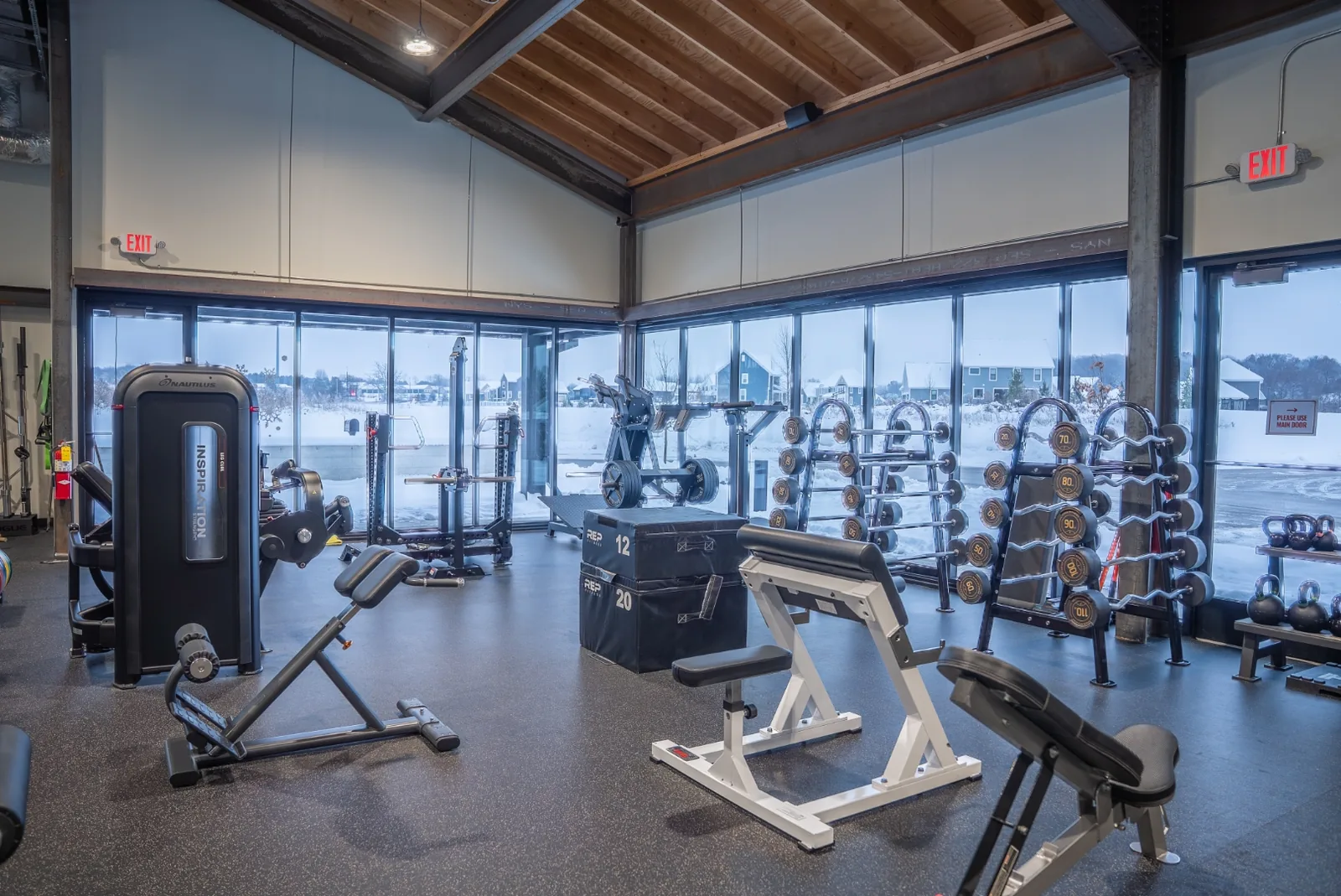 A squat rack and open lifting area at VirtueHall, with adjustable benches and natural light from floor-to-ceiling windows